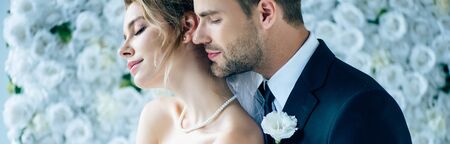 panoramic shot of attractive bride and handsome bridegroom hugging with closed eyesの写真素材