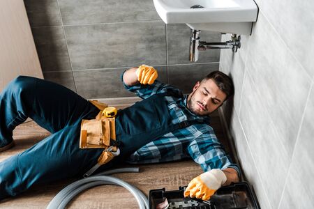 bearded handyman lying on floor near toolbox in bathroomの写真素材