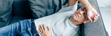 panoramic shot of handsome man with stomachache in apartment