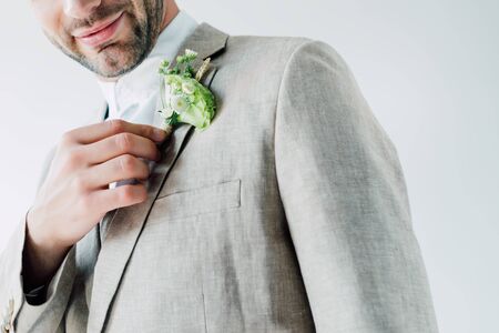 cropped view of bridegroom in suit holding floral boutonniere isolated on greyの写真素材