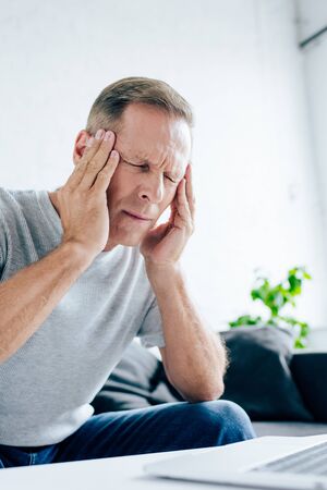 handsome man in t-shirt with closed eyes touching head in apartment