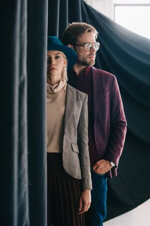 elegant young woman in hat and man in glasses near curtainの写真素材