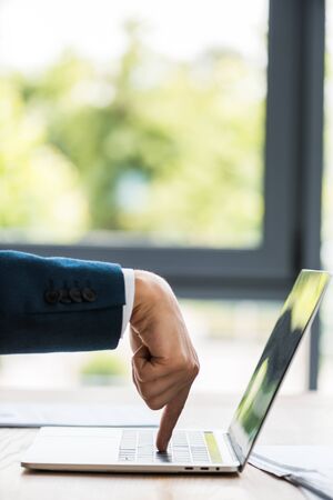 cropped view of businessman pointing with finger at laptop keyboardの写真素材