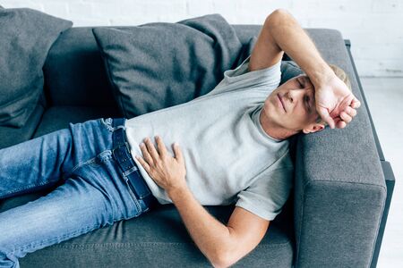 handsome man in t-shirt with stomachache lying on sofaの写真素材