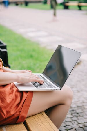 cropped view of woman sitting on bench and using laptop with blank screenの写真素材