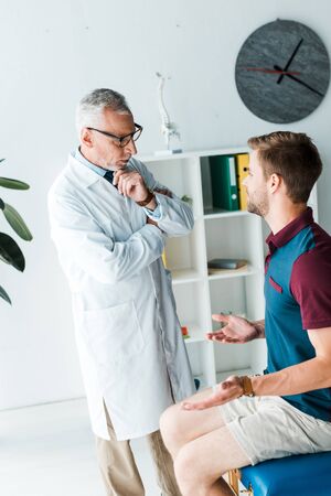 pensive doctor in glasses looking at man showing shrug gestureの写真素材