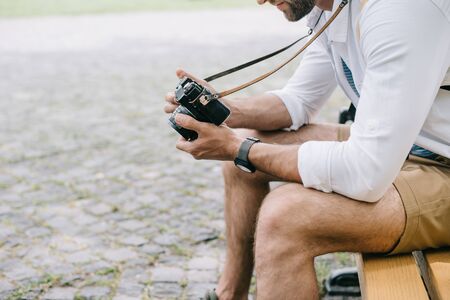 cropped view of bearded man sitting on bench with digital cameraの写真素材