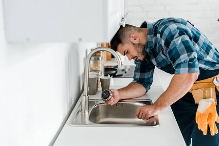 selective focus of handsome bearded repairman working near sink in kitchenの写真素材