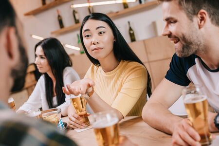 selective focus of young asian woman gesturing while sitting with friends in pubの写真素材
