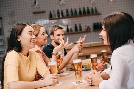 cheerful multicultural friends talking while drinking beer together in pubの写真素材
