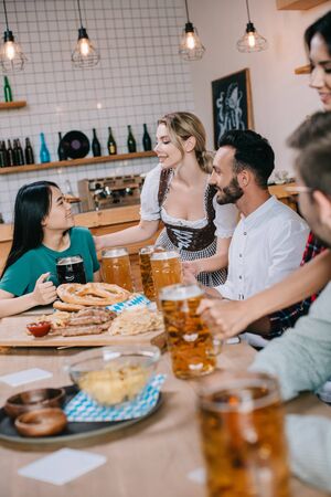 two waitresses in traditional german costume serving beer for multicultural friends in pubの写真素材