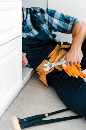 cropped view of repairman holding adjustable wrench near kitchen cabinet