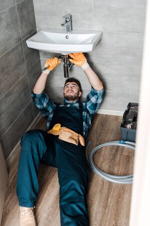 handsome repairman fixing water damage with adjustable wrench in bathroom