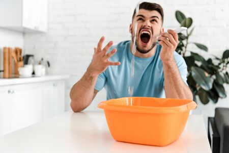 selective focus of bearded man screaming while looking at water pouring into plastic wash bowlの写真素材