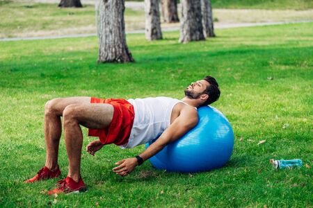 handsome bearded man working out on fitness ball near sport bottleの写真素材