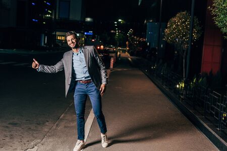 handsome businessman in formal wear thumbing and smiling in night cityの写真素材