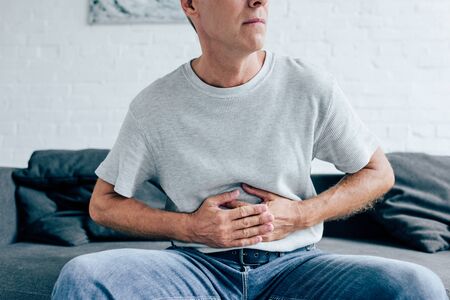cropped view of man in t-shirt with stomachache in apartmentの写真素材
