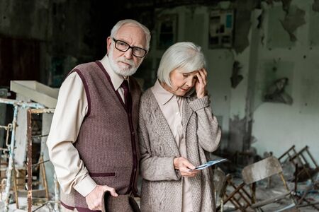 retired couple standing in abandoned school and holding photoの写真素材