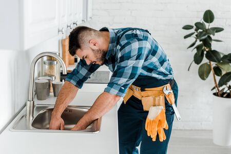 handsome bearded repairman working near sink in kitchenの写真素材
