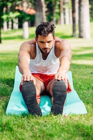 selective focus of handsome sportsman doing stretching exercise on fitness mat