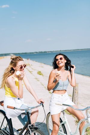 happy girls riding bikes with ice cream near river in summerの写真素材