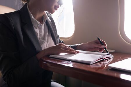 cropped view of businesswoman working with documents in plane during business trip