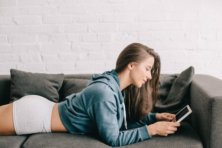 beautiful woman in panties using digital tablet while lying on sofaの写真素材