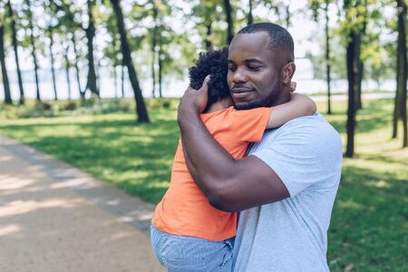 happy african american father holding and embracing adorable son in parkの写真素材