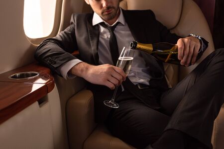 cropped view of man pouring champagne into glass in planeの写真素材