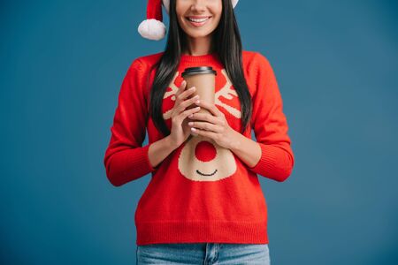 cropped view of happy woman in santa hat holding coffee to go, isolated on blueの写真素材