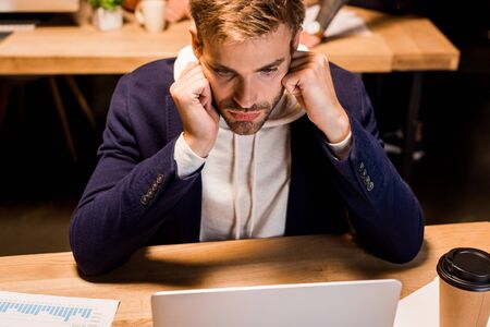 young, tired businessman looking at laptop while working at night in office