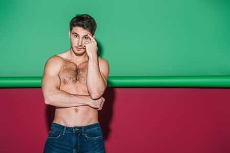 sexy shirtles man in denim jeans looking at camera on green and red background