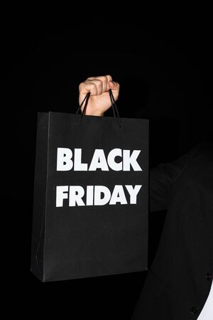 partial view of man holding shopping bag with black friday sign, isolated on blackの写真素材