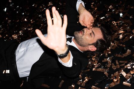 smiling man lying on floor with golden confetti for holiday