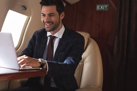 cheerful businessman working with laptop in plane during business trip