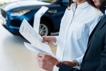 cropped view of woman and man holding papers with lettering in car showroom の写真素材