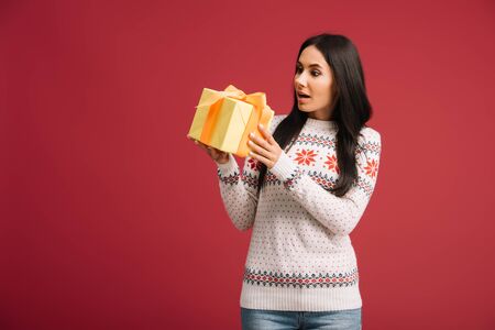 beautiful shocked woman holding christmas present isolated on redの写真素材