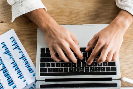 partial view of businessman using laptop near paper with graphs and chartsの写真素材