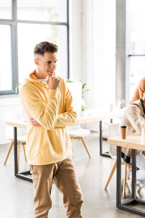 young, smiling businessman standing in office and holding hand near faceの写真素材