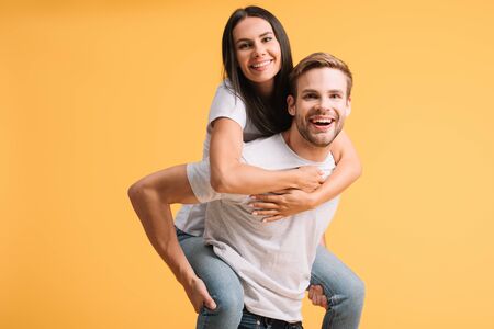 beautiful happy couple piggybacking in white t-shirts, isolated on yellowの写真素材