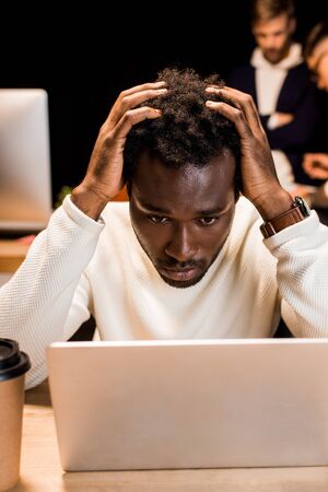 tired african american businessman holding hands on head while working at night in office