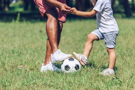 cropped view of african american father and son playing football in parkの写真素材