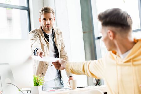 selective focus of young businessman giving paper to colleague in office