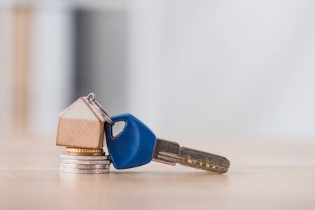 key with toy house trinket on stack of holden and silver coins on wooden table