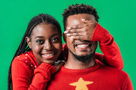 African American woman in red sweater covering eyes with hand to man isolated on green