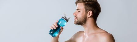 panoramic shot of shirtless bearded sportsman holding sport bottle isolated on greyの写真素材