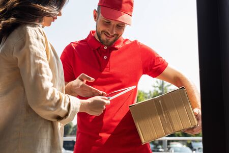 cheerful delivery man gesturing while looking at digital tablet near womanの写真素材