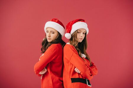 attractive and sad women in sweaters and santa hats looking down isolated on redの写真素材