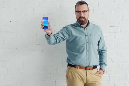 handsome businessman with hand in pocket holding smartphone with block screen