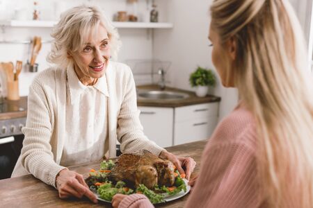 smiling mother and daughter holding plate with turkey in Thanksgiving dayの写真素材